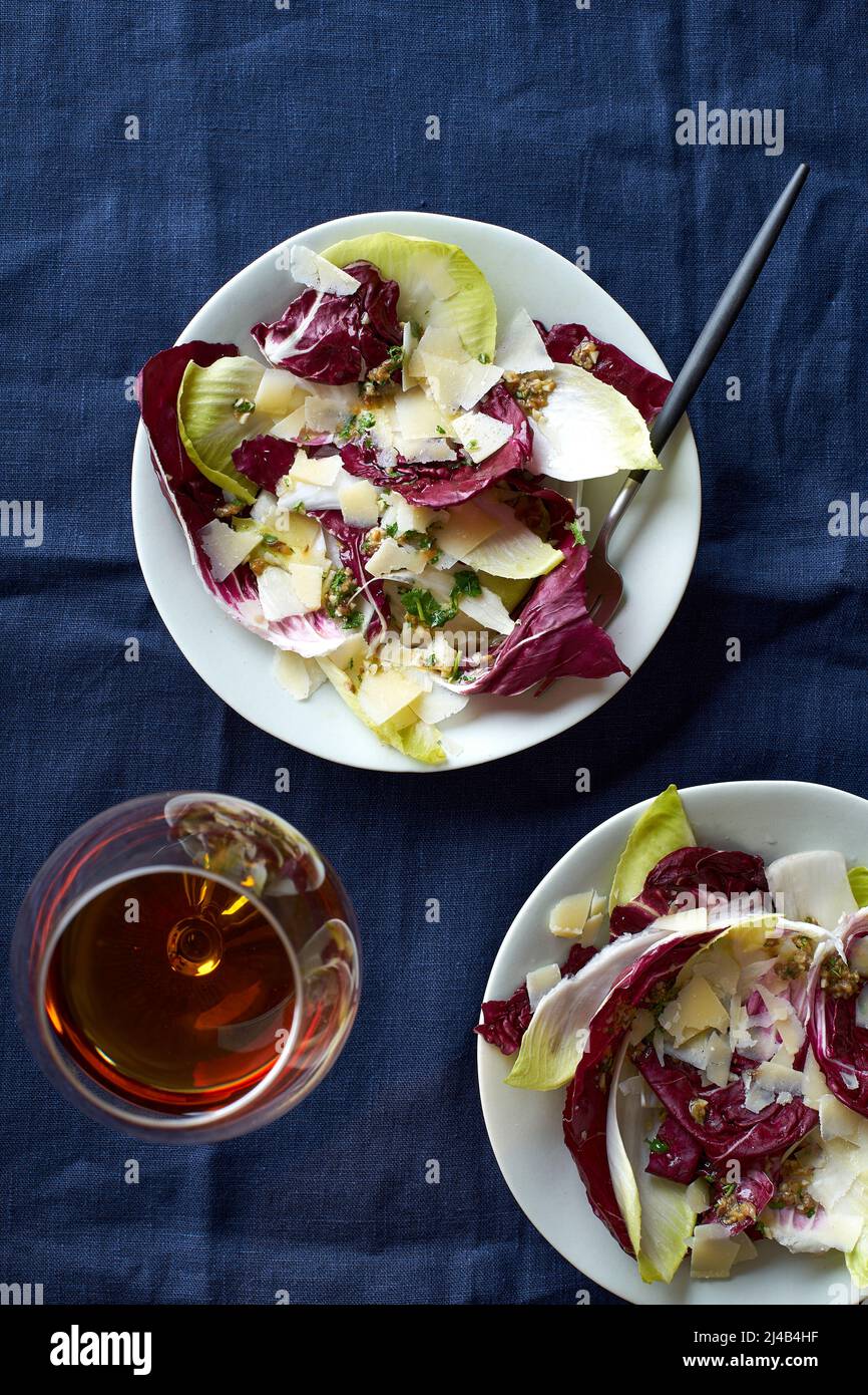 Salade au radicchio, chicorée et parmesan servie avec un verre de vin orange sur fond bleu Banque D'Images