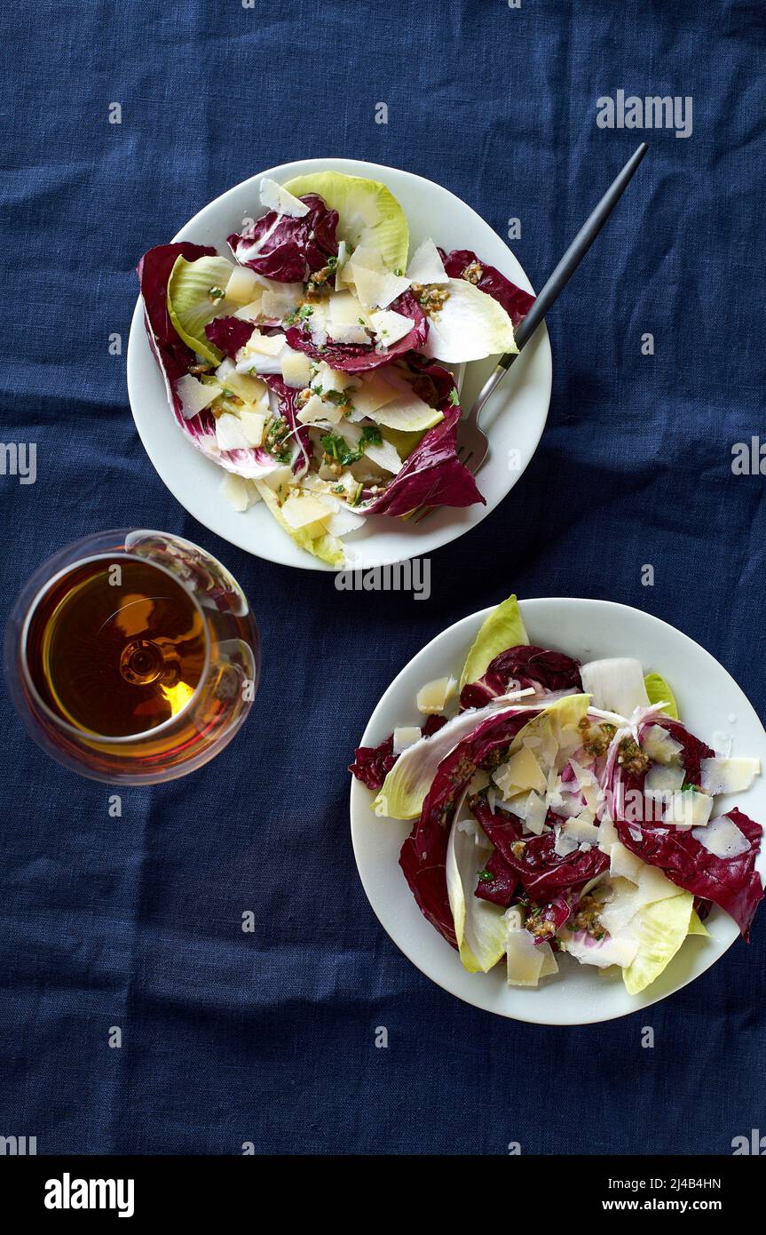 Salade au radicchio, chicorée et parmesan servie avec un verre de vin orange sur fond bleu Banque D'Images