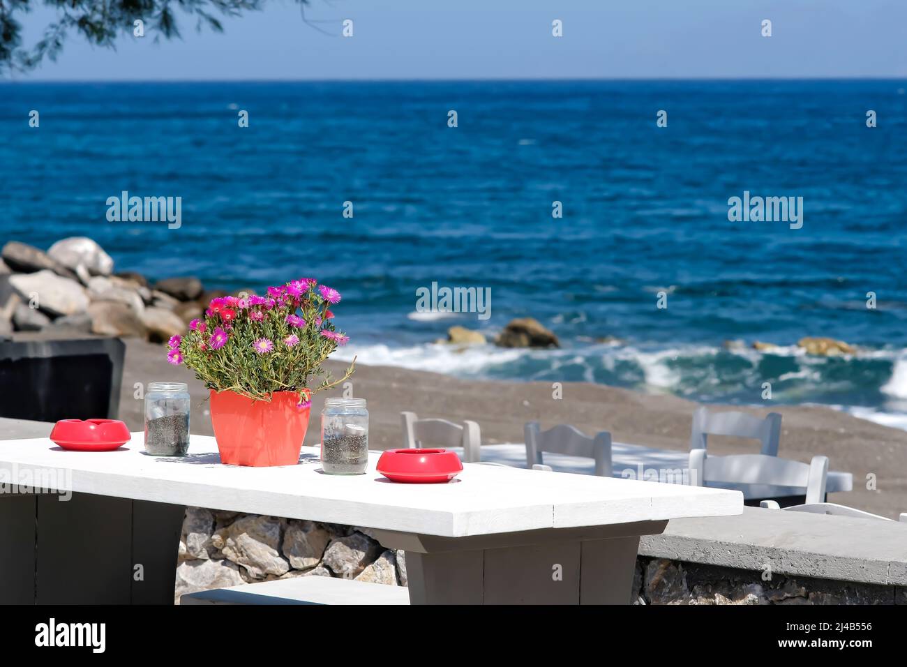 Un beau bar extérieur décoré de fleurs et de cendriers avec une vue imprenable sur la célèbre plage de Perissa à Santorin Banque D'Images