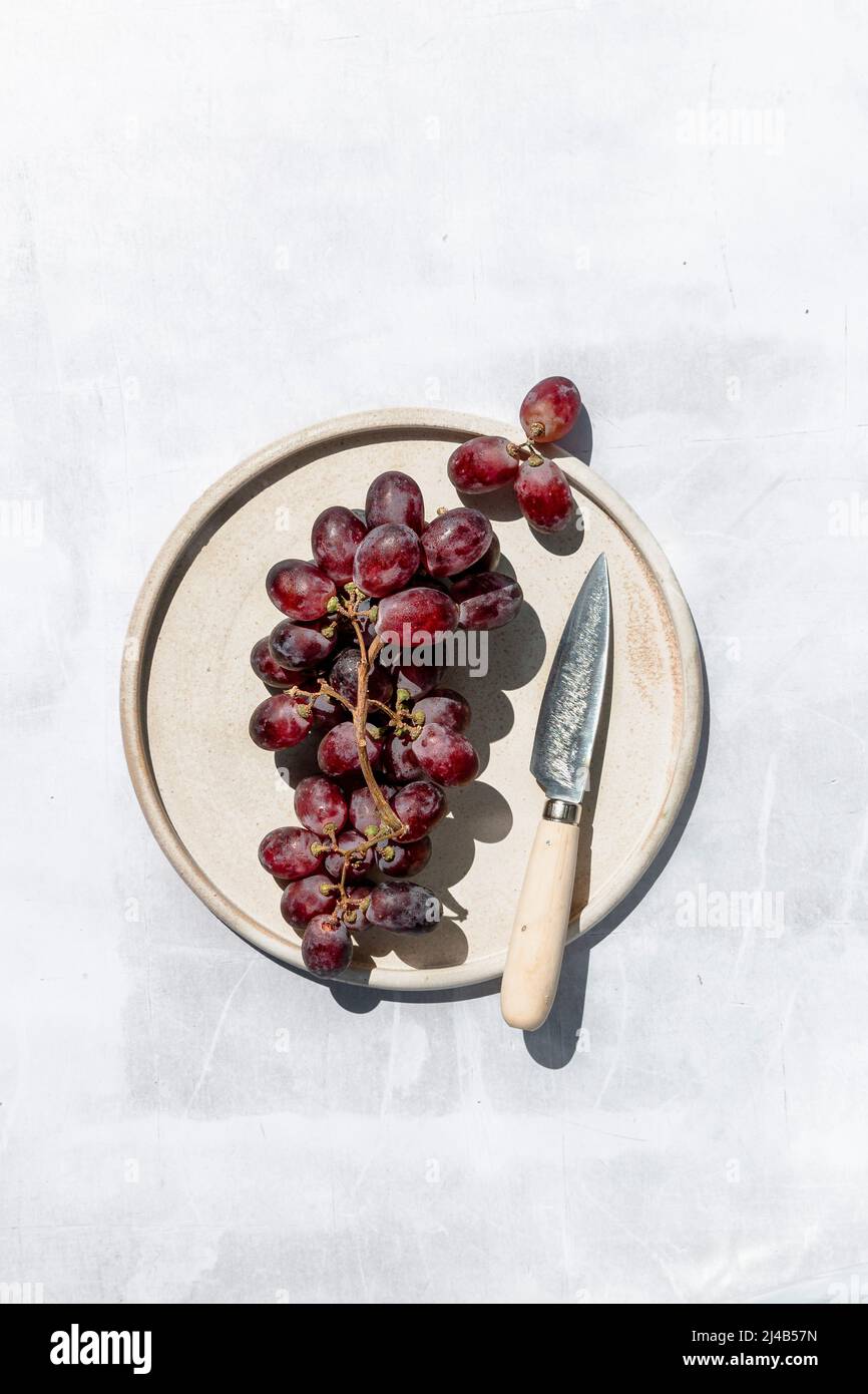 Bouquet de raisins rouges sur une plaque de céramique, avec un couteau. Banque D'Images