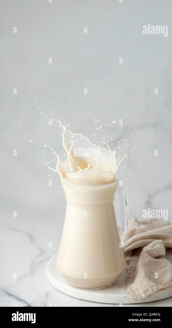 Le lait végétal végétalien sans produits laitiers éclabousse dans un pot en verre sur fond de marbre blanc. Copier l'espace. Verticale Banque D'Images