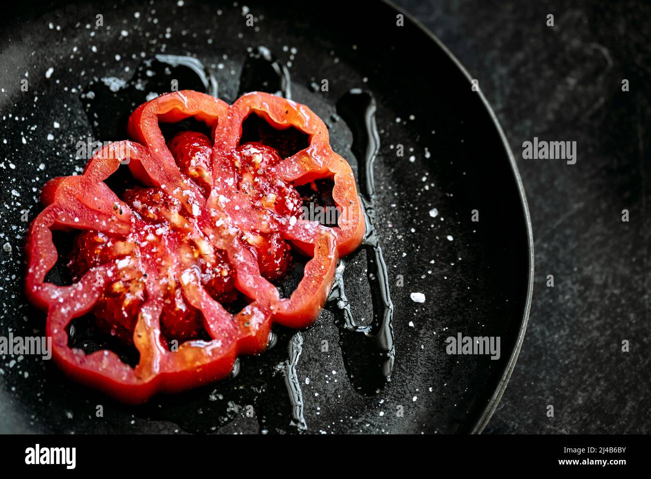 tranche de tomate coeur de boeuf, placée sur une assiette noire, sel, poivre et huile d'olive, sur fond noir texturé. vue d'en haut Banque D'Images
