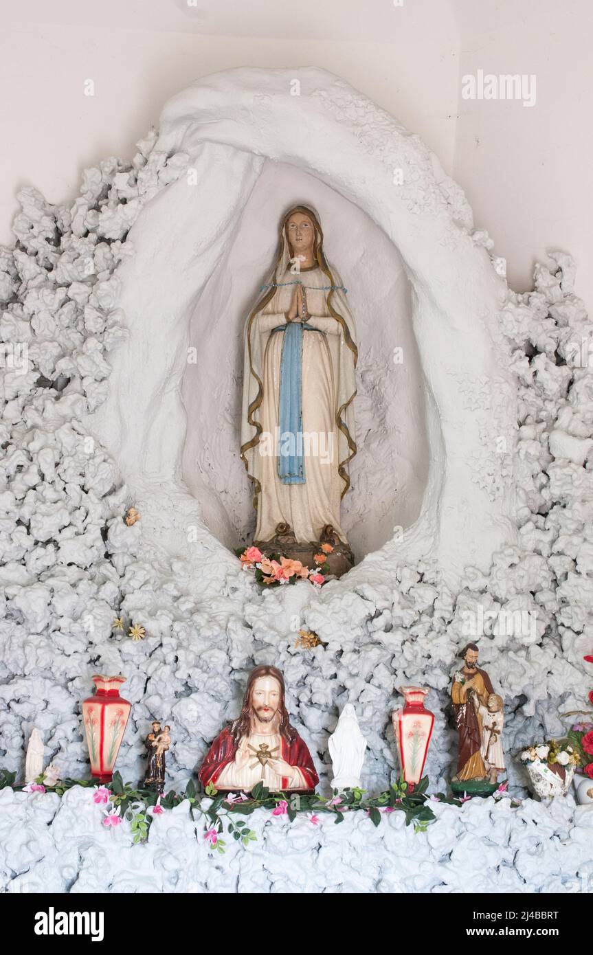 Chapelle catholique avec la sainte Marie et Jésus dans une grotte blanche entourée de saints et de fleurs en plastique. Banque D'Images