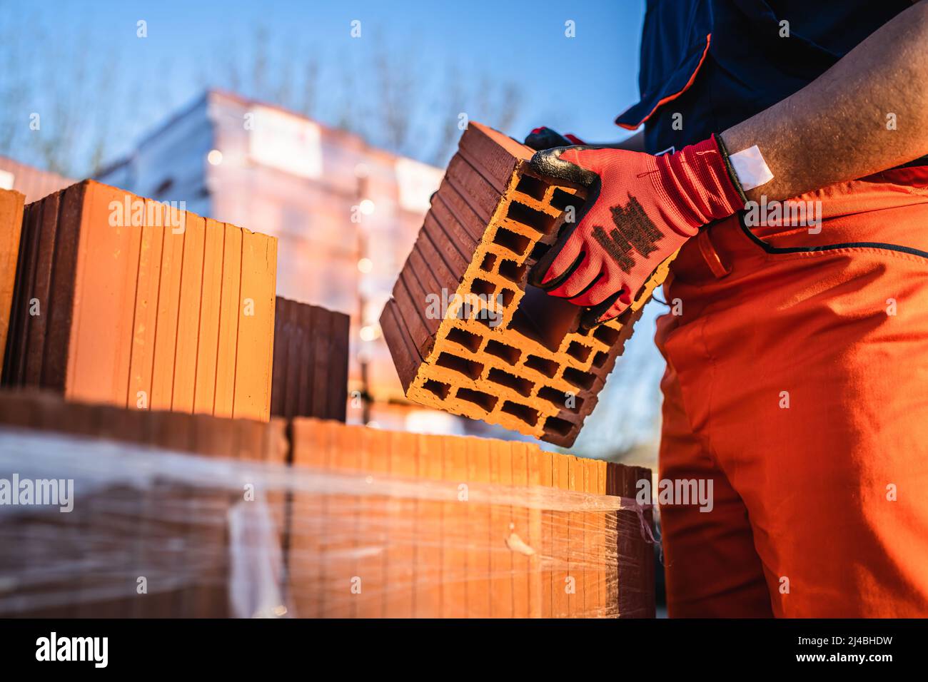 Gros plan sur les mains de l'homme inconnu ouvrier de construction prenant argile brique orange bloc creux argile pour la construction à l'entrepôt ou le chantier de construction dans sunn Banque D'Images