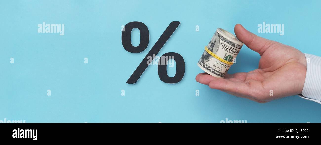 Une main avec des dollars roulés dans un tube pointe vers le symbole de pourcentage. Banque D'Images