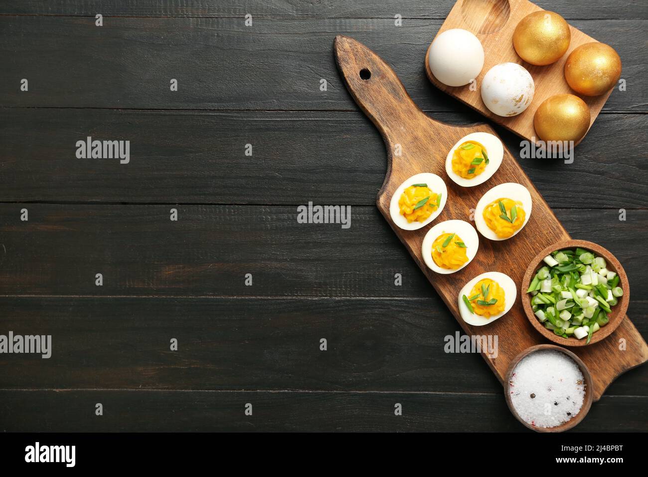 Planche, support avec œufs de Pâques, épices et oignon vert sur fond de bois foncé. Fête de Pâques Banque D'Images