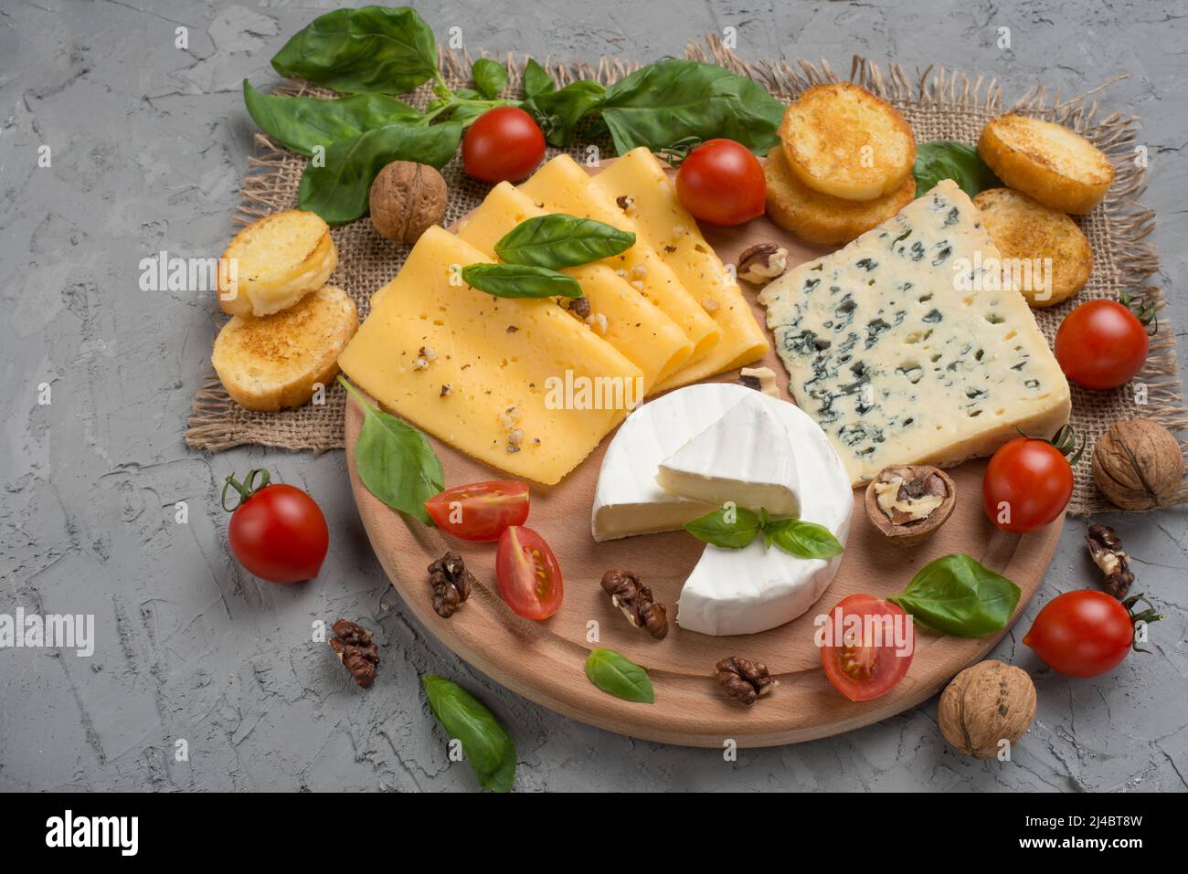 Différents types de fromages, avec basilic, tomates cerises, croûtons de baguettes. Banque D'Images