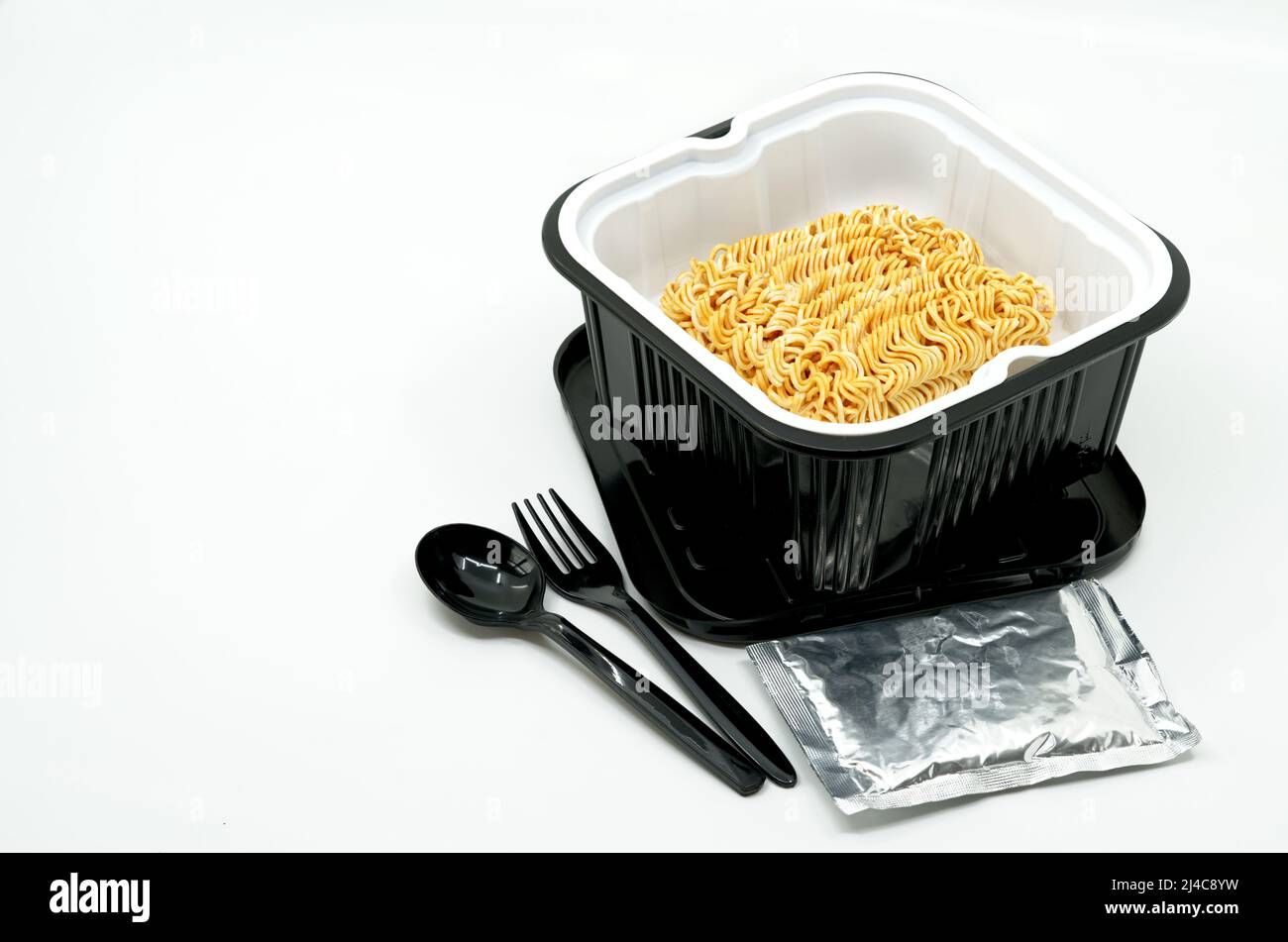 Nouilles instantanées dans un bol en plastique noir avec cuillère et fourchette en plastique noir, ingrédients dans un petit paquet de folie, soupe instantanée de nouilles à chaud automatique par po Banque D'Images