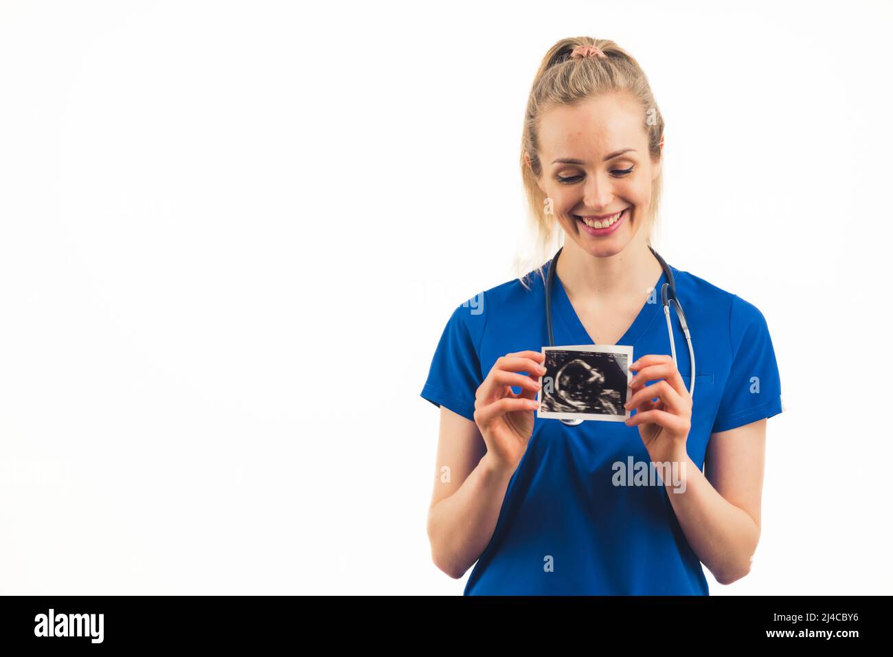 Jeune femme blonde caucasienne médecin tenant le dépistage d'ultrasons prénatal et souriant. Studio moyen tourné sur fond blanc. Photo de haute qualité Banque D'Images