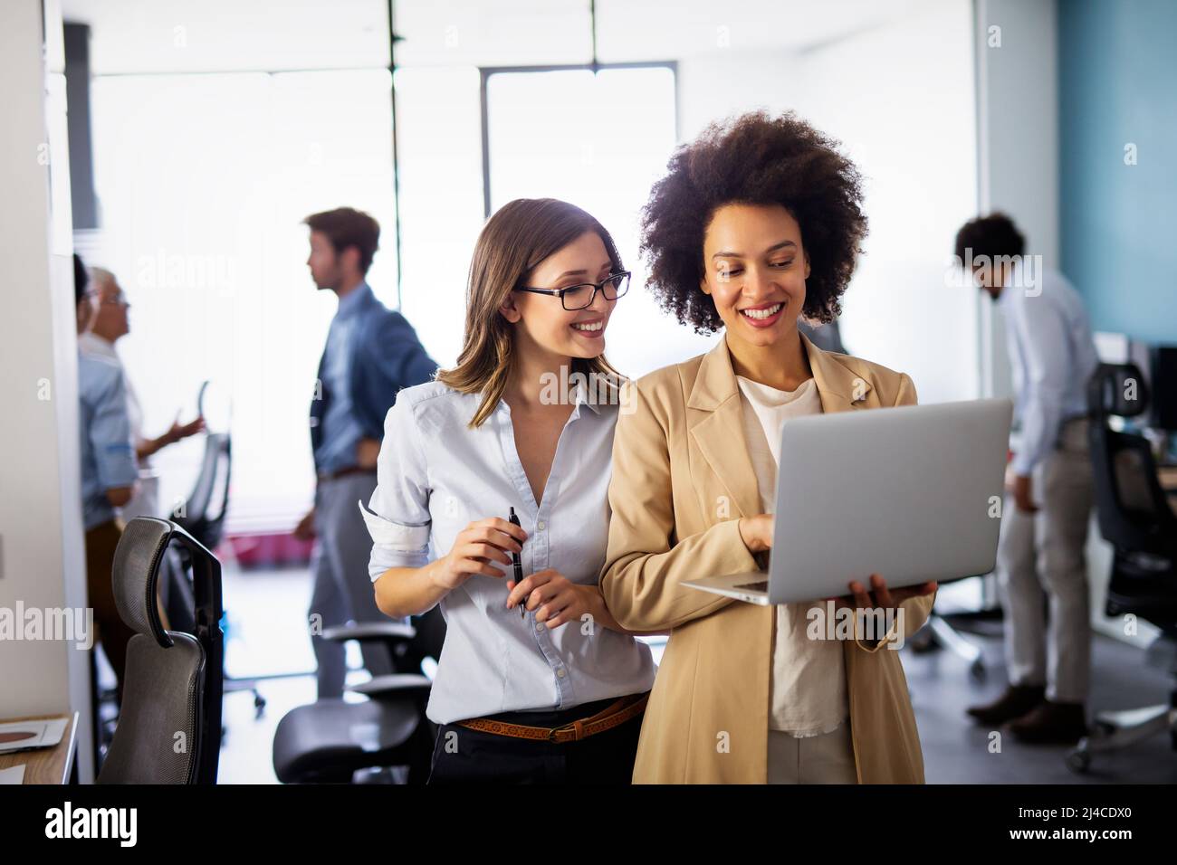 Des femmes d'affaires multiethniques heureuses travaillant ensemble en ligne sur un ordinateur portable dans un bureau d'entreprise. Banque D'Images
