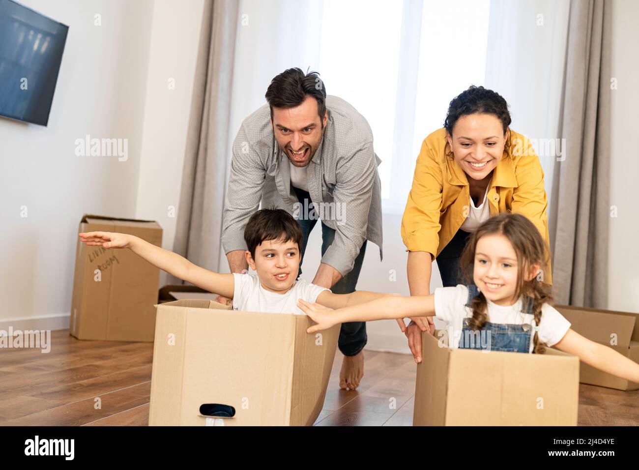 Les familles multiraciales de quatre personnes s'amusent dans une nouvelle  maison, les parents emportant des enfants dans des boîtes en carton dans un  salon vide, les enfants heureux se répandant les bras