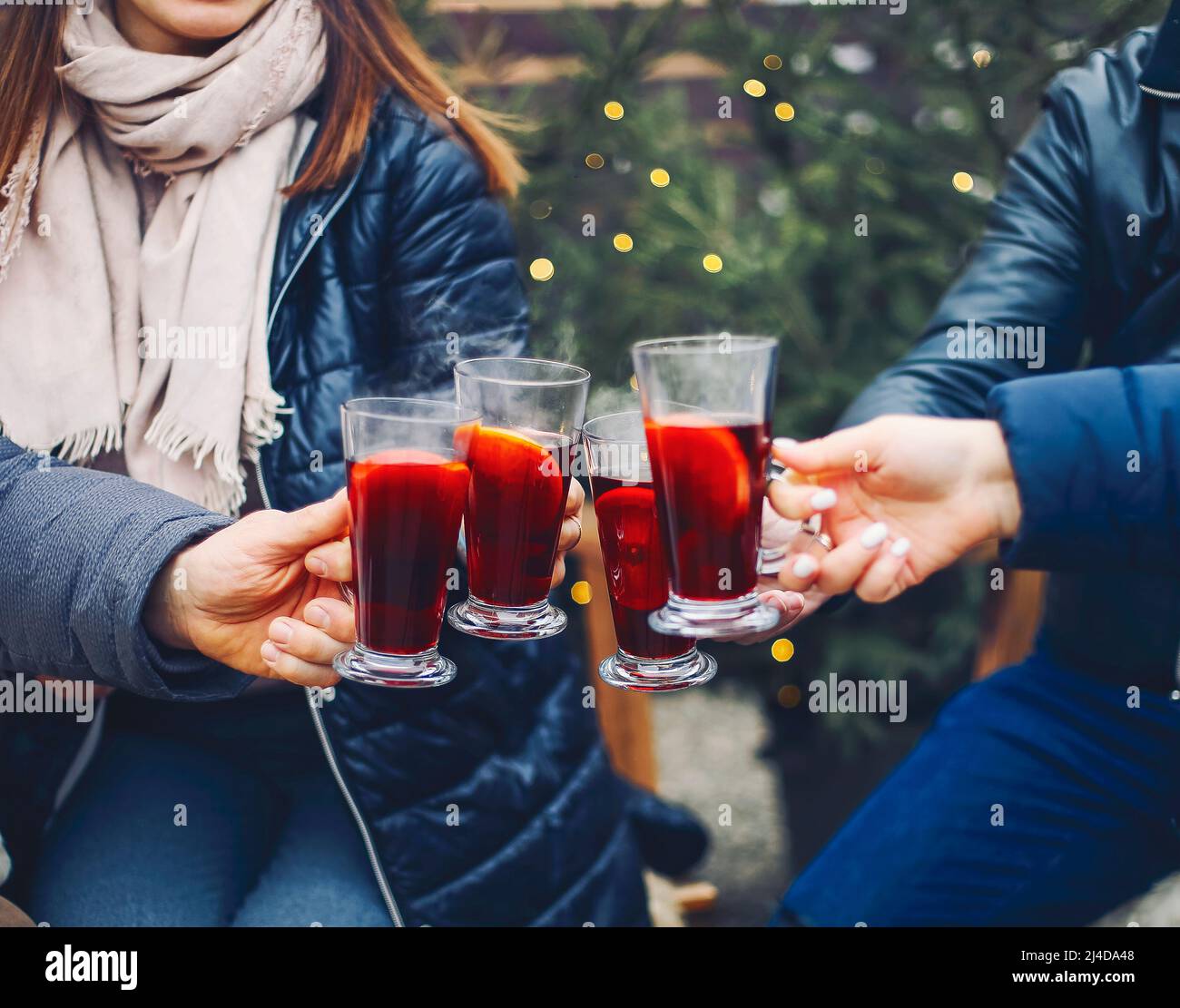 Amis qui boivent un délicieux vin chaud lors de la fête. Prise de vue d'un groupe de jeunes amis joyeux s'amusant et appréciant une boisson chaude sur le marché de Noël A. Banque D'Images