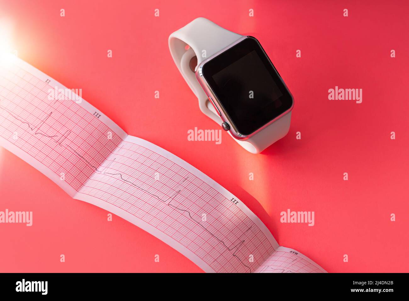 Montre intelligente sur bande en silicone blanc, papier de schéma ECG sur fond de corail rose. Examen médical du cardiogramme. Prévenir la maladie des coeurs, mitral Banque D'Images