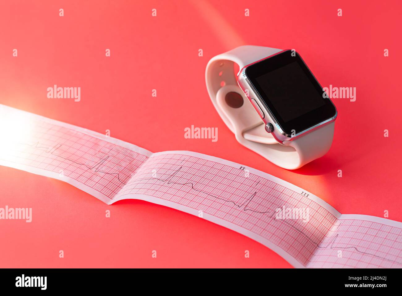 Montre intelligente sur bande en silicone blanc, papier de schéma ECG sur fond de corail rose. Examen médical du cardiogramme. Prévenir la maladie des coeurs, mitral Banque D'Images