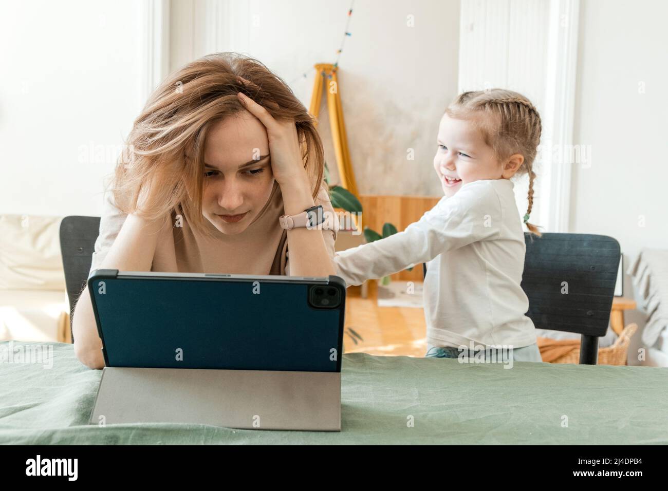 Mère essayant de travailler de la maison sur une tablette avec sa fille. Quarantaine et travail à distance pendant l'épidémie de coronavirus. L'enfant fait du bruit et moi Banque D'Images