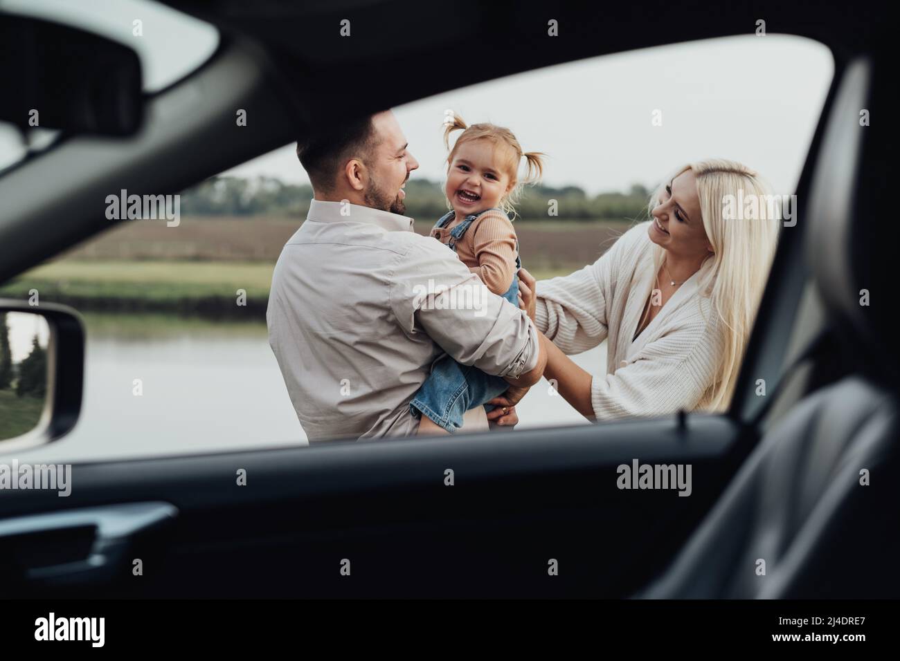 Vue à travers la fenêtre à l'intérieur de la voiture, Happy Young Family, maman et papa avec leur petite fille s'amuser ensemble et profiter du week-end à l'extérieur de la Banque D'Images