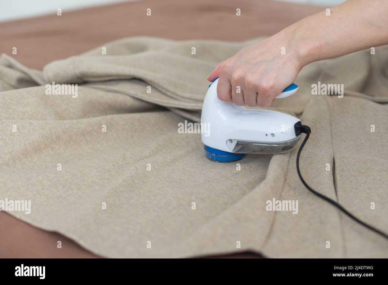 Dispositif sans fil pour le nettoyage des tissus tricotés contre les peluches. La femme retire les peluches du pull. Banque D'Images