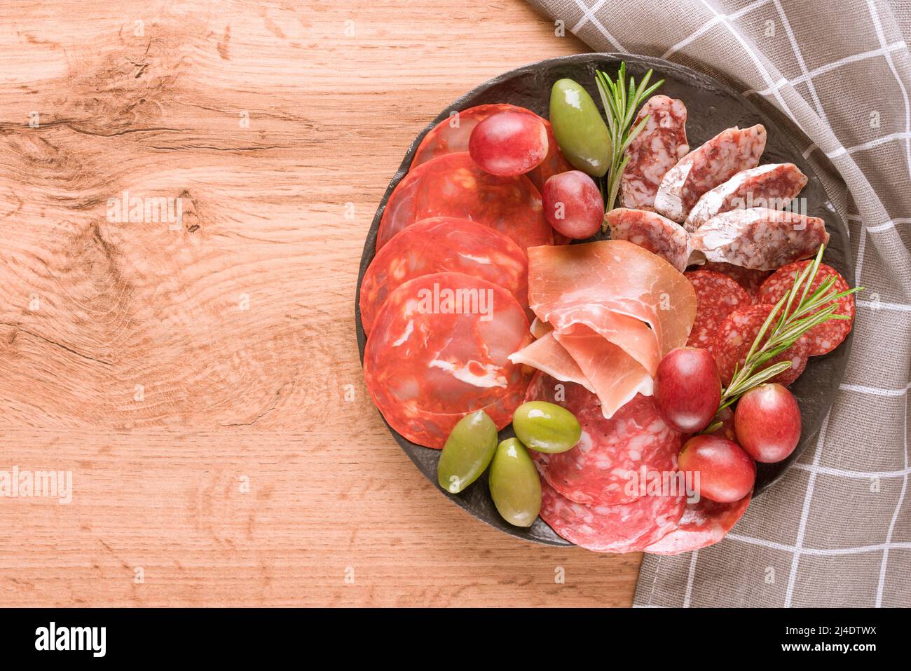 Vue de dessus sur l'assiette de charcuterie avec différents types de saucisses - salami, bresaola, prostcuitto servi avec des olives et du raisin. Assiette noire avec tradition Banque D'Images
