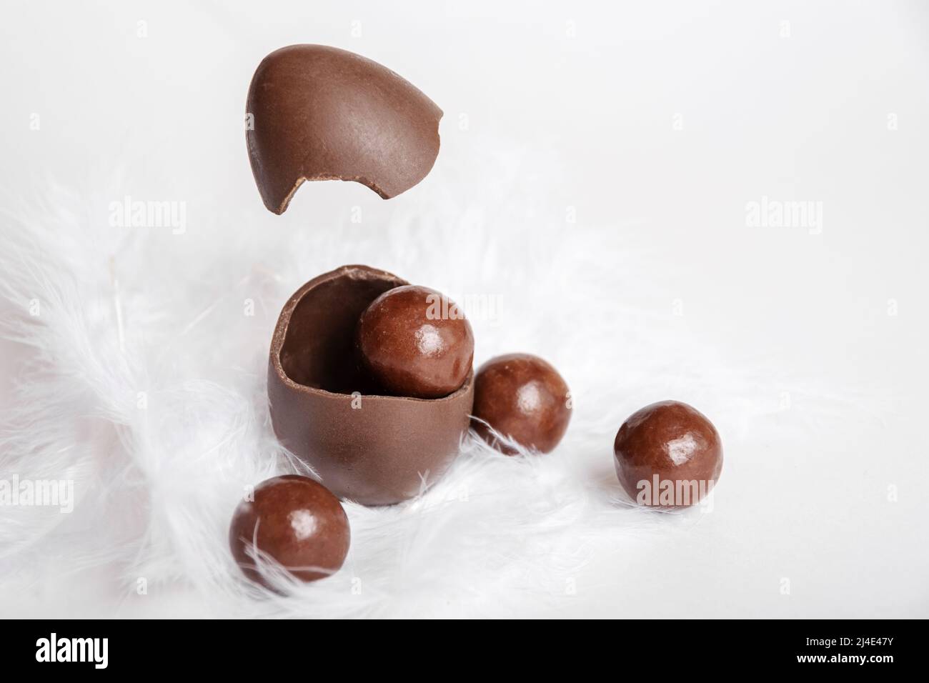 Œuf de pâques au chocolat fissuré avec de petits bonbons ronds au chocolat et coquille d'œuf volante dans un nid de plumes blanches, espace de copie, lévitation. Gâteries au chocolat Banque D'Images