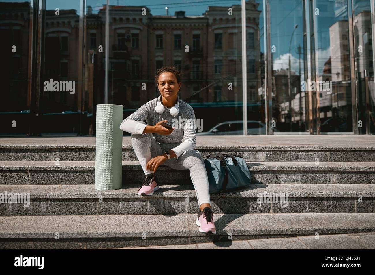 Jeune femme en tenue active regardant la caméra tout en étant assise sur les escaliers Banque D'Images