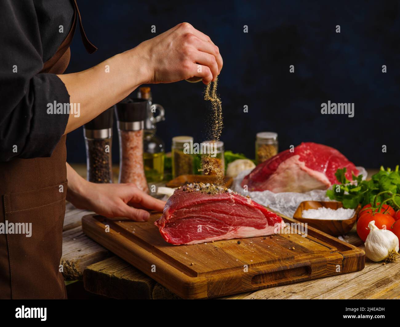 Un chef professionnel prépare un plat de gros morceau de bœuf, de veau sur une planche à découper en bois sur fond sombre. Viande, herbes, sel et épices sur un W. Banque D'Images