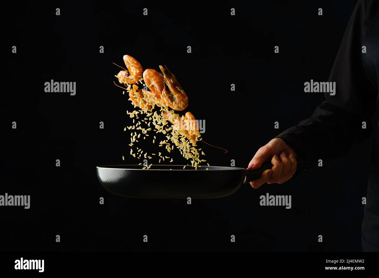 Crevettes tigrées dans une casserole dans un vol gelé sur fond noir dans la main du chef. Cuisine de fruits de mer, cuisine asiatique, plats gastronomiques. Végétarien sain Banque D'Images