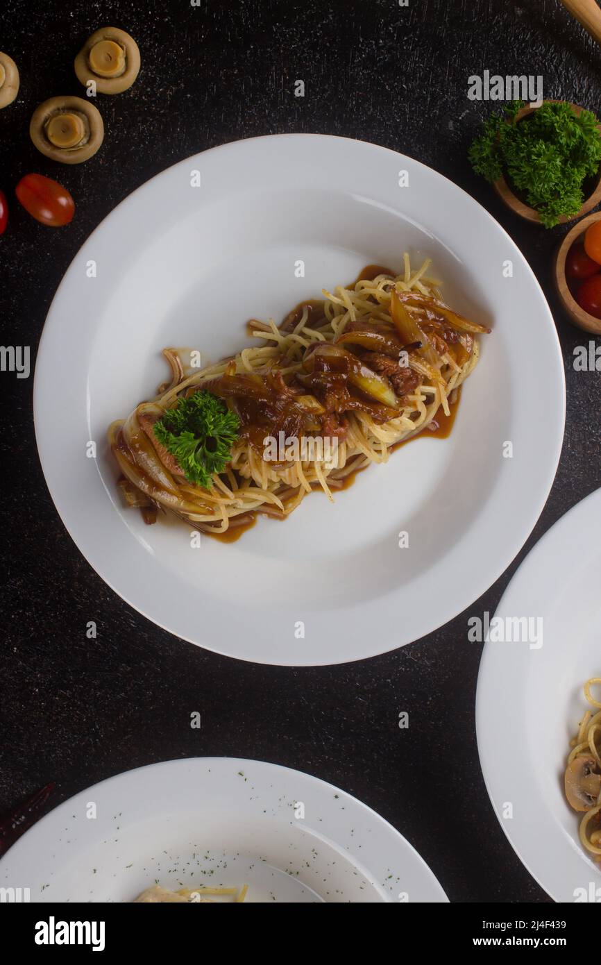 un spaghetti cuit aux pâtes avec sauce au poivre noir, une tranche de bœuf, de l'huile d'olive et du persil vert frais dans une assiette ovale blanche avec ingrédients Banque D'Images