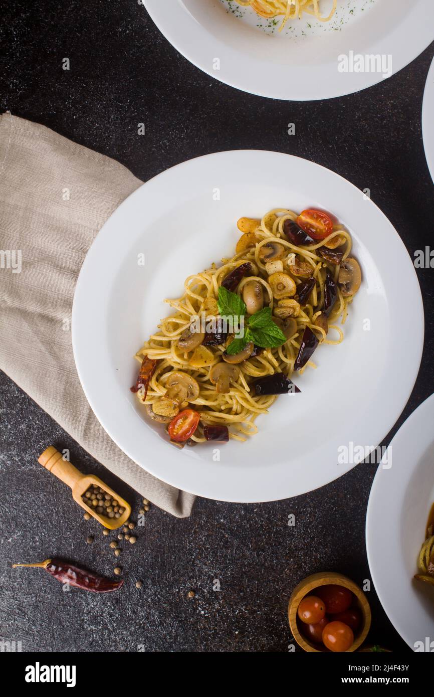 un spaghetti cuit aux pâtes avec sauce aux champignons, une tranche de bœuf, de l'huile d'olive et du persil vert frais dans une assiette ovale blanche avec des ingrédients sur fond noir Banque D'Images
