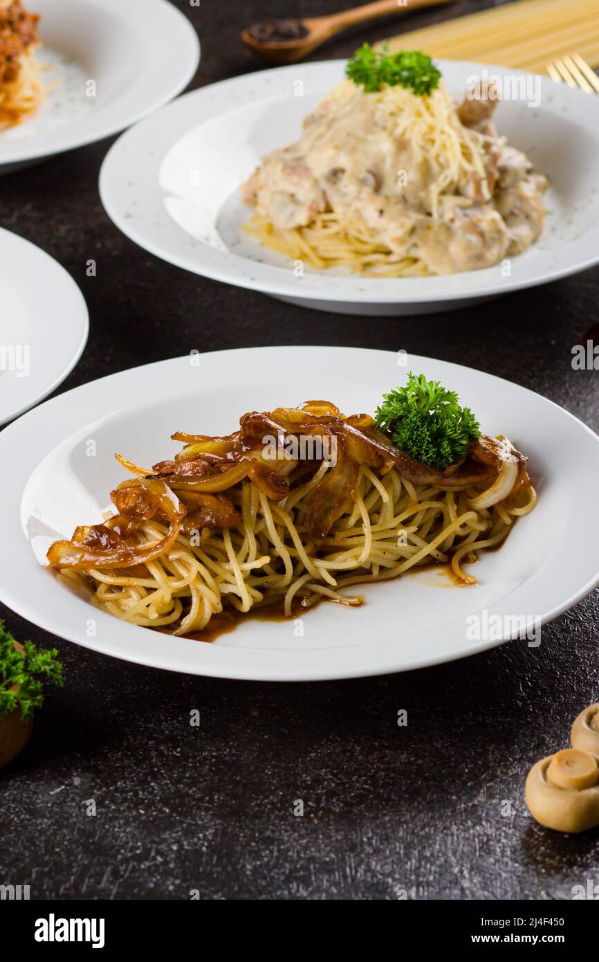 un spaghetti cuit aux pâtes avec sauce au poivre noir, une tranche de bœuf, de l'huile d'olive et du persil vert frais dans une assiette ovale blanche avec ingrédients Banque D'Images