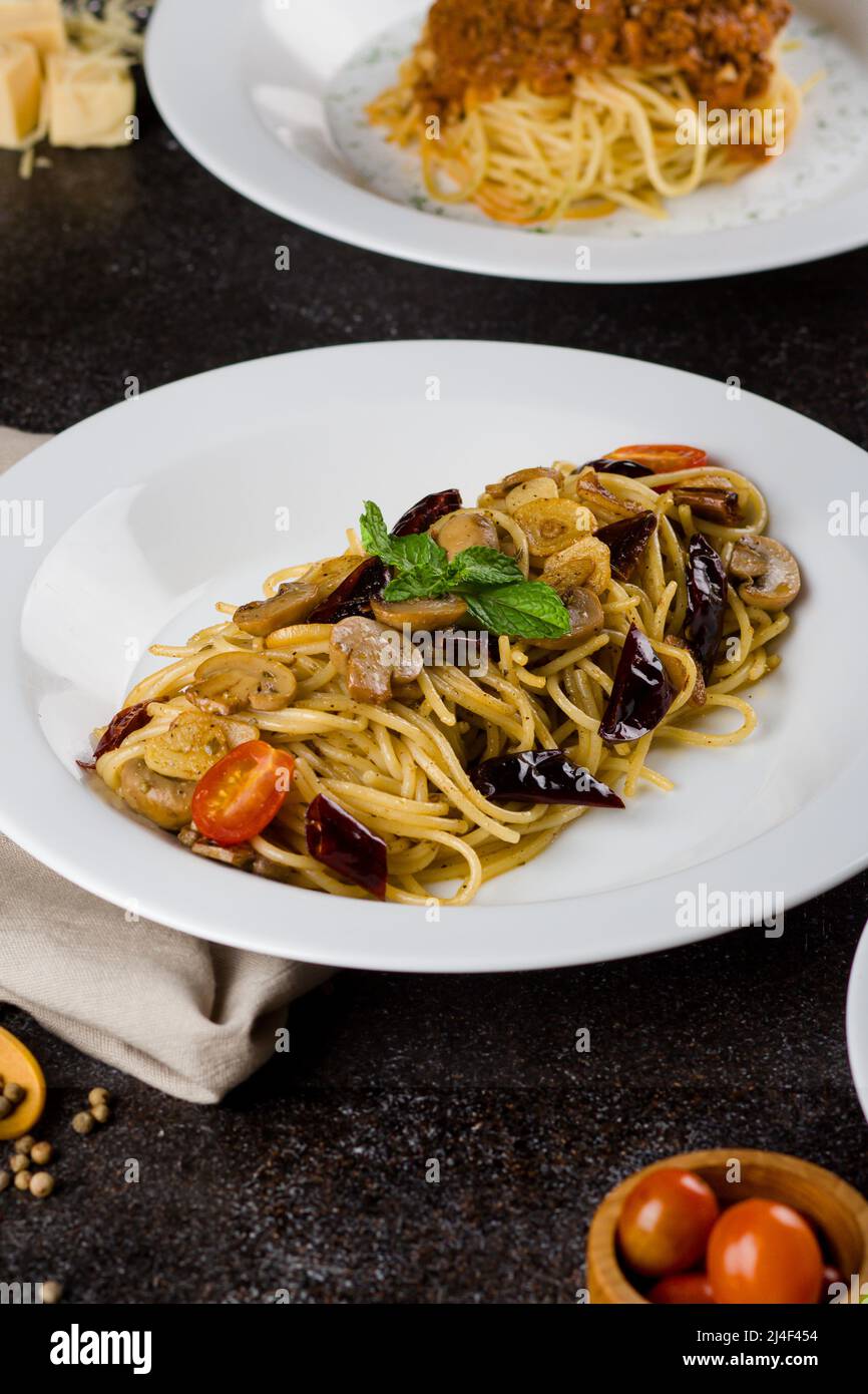 un spaghetti cuit aux pâtes avec sauce aux champignons, une tranche de bœuf, de l'huile d'olive et du persil vert frais dans une assiette ovale blanche avec des ingrédients sur fond noir Banque D'Images