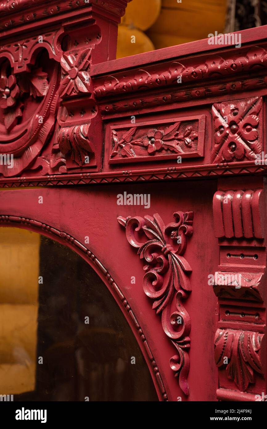 Gros plan de l'ancienne armoire ornementée rénovée peinte en rouge avec des murs de maison en bois en arrière-plan. Restauration de meubles anciens à la maison par Banque D'Images