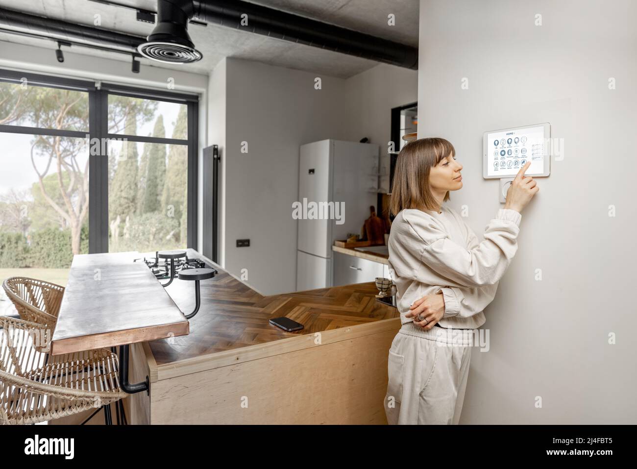 Femme contrôlant des appareils domestiques avec un Smart Panel numérique fixé au mur Banque D'Images