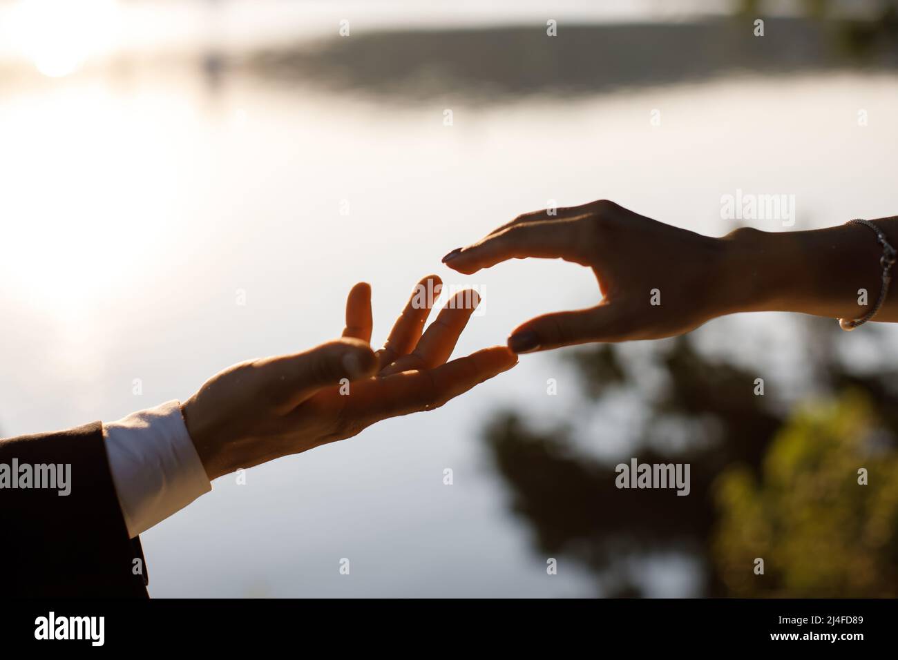 La mariée atteint le marié avec la toile de fond d'un beau lac au coucher du soleil Banque D'Images