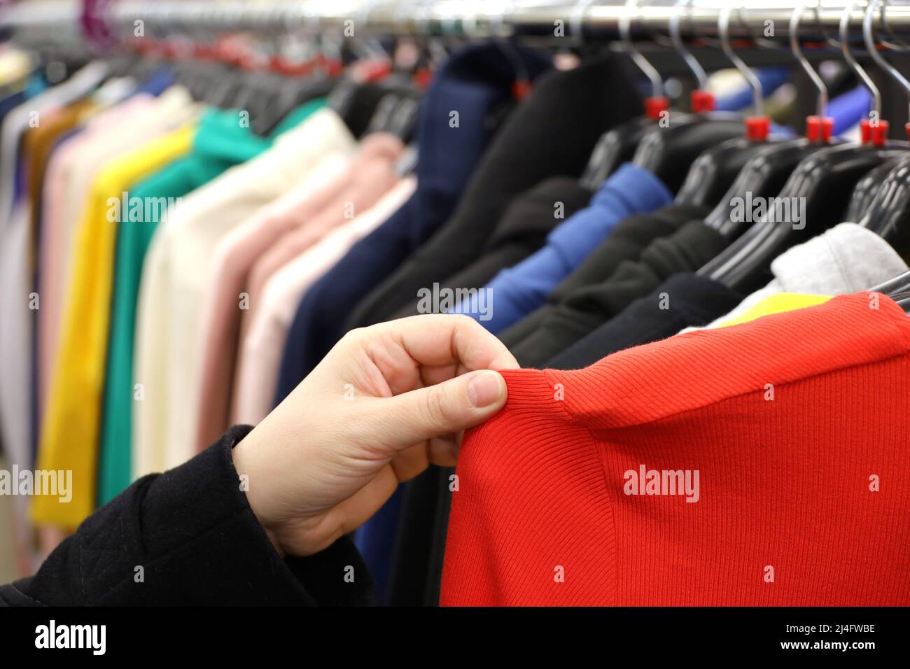 Femme choisissant un chemisier rouge dans un magasin de vêtements. Différents vêtements pour femmes sur un rack Banque D'Images