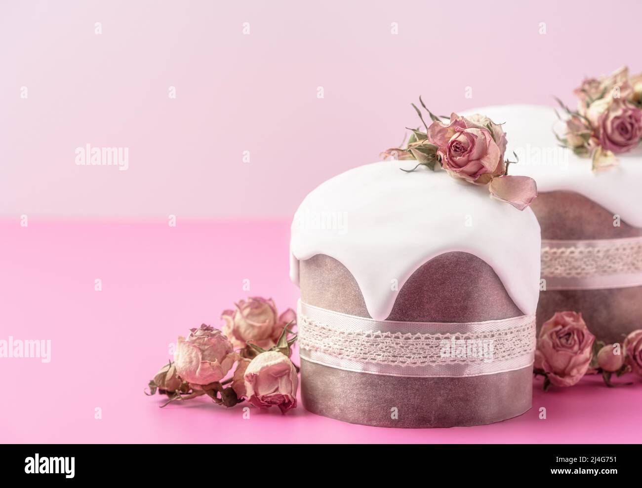 Gâteaux de Pâques vitrés décorés de fleurs de rose de thé sur fond rose vif. Composition de Pâques avec gâteaux, roses et œufs au chocolat. Arrière-plan de vacances avec espace de copie pour votre conception. Banque D'Images