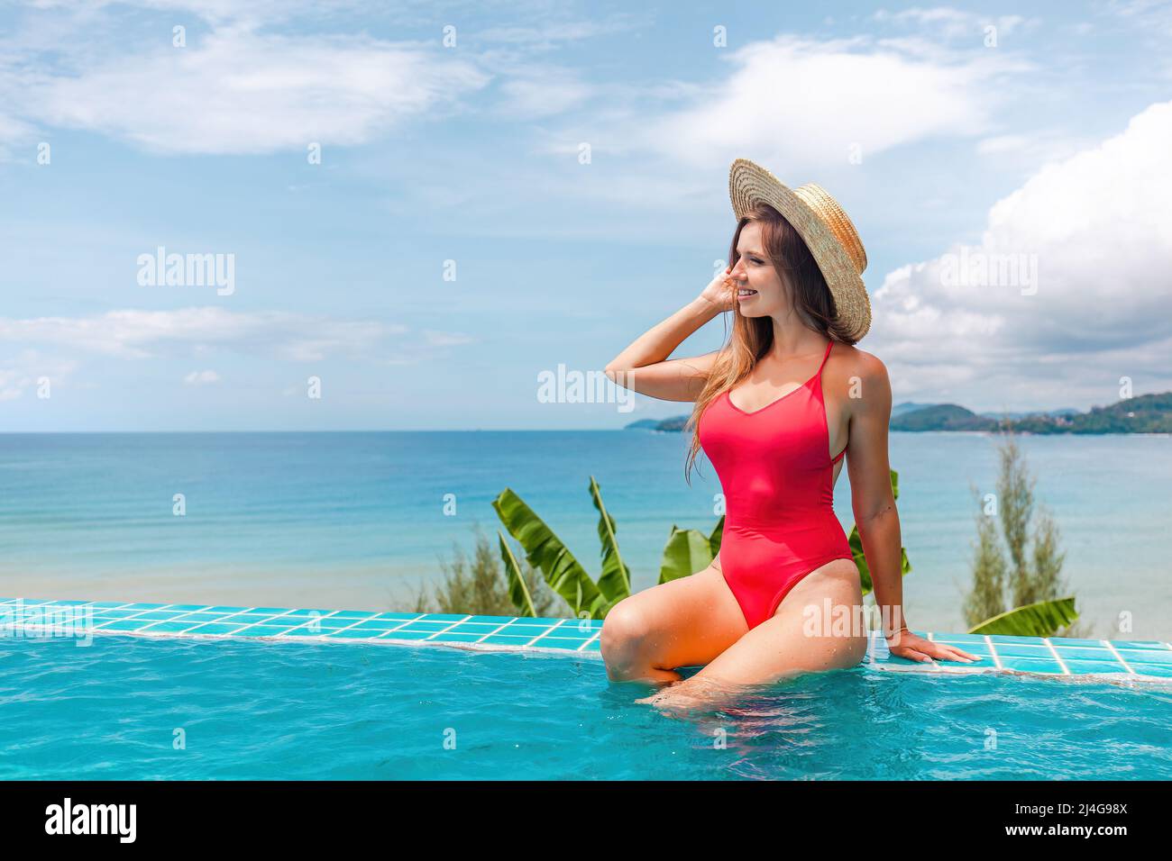 Femme en maillot de bain rouge se détendre dans la piscine avec vue sur la mer. Vacances tropicales Banque D'Images