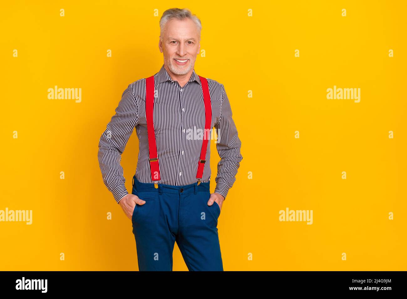 Portrait d'homme imposant gai attrayant tenant les mains dans les poches posant isolé sur fond jaune vif Banque D'Images