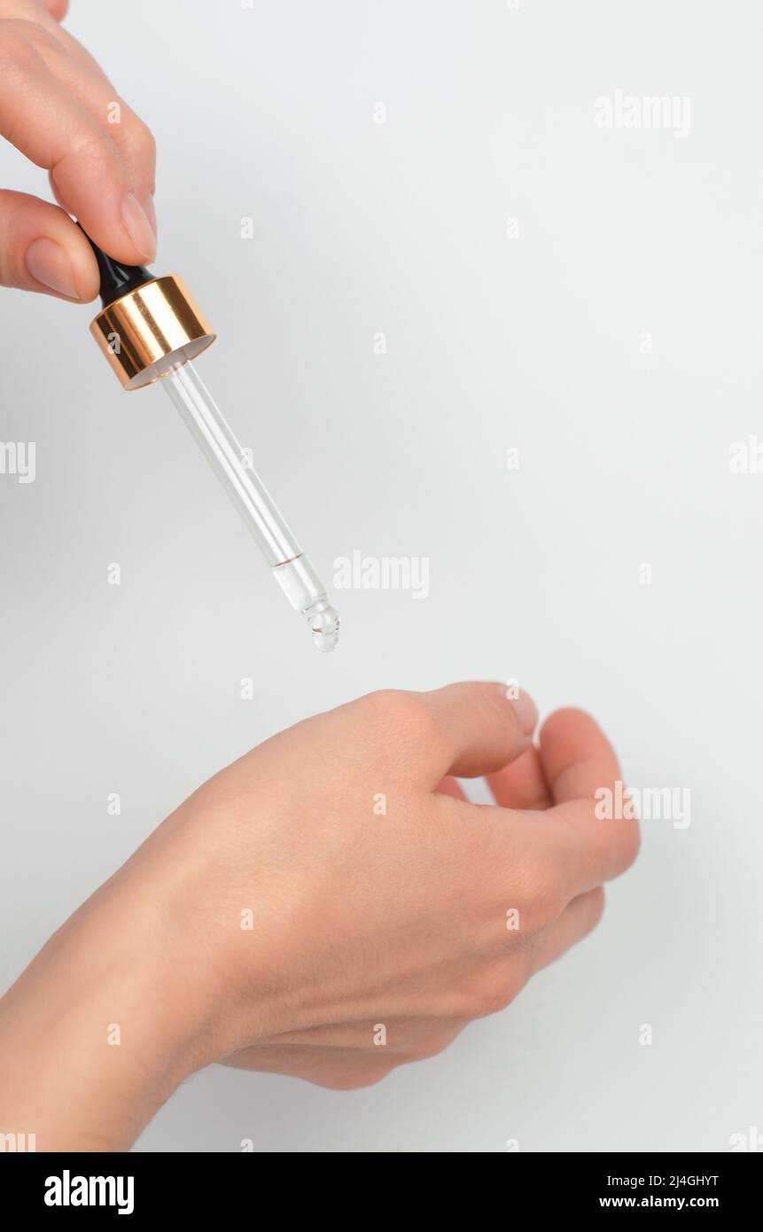 Une pipette en verre dans la main d'une femme goutte l'huile essentielle sur sa main. Procédures cosmétiques Banque D'Images