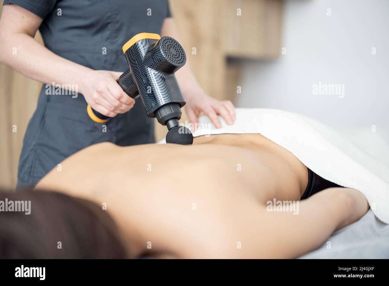 La femme fait un massage du dos du patient à l'aide d'un masseur à percussion Banque D'Images