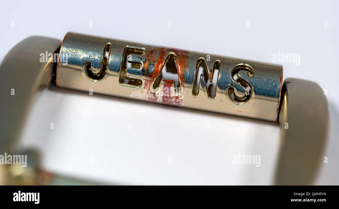 Vue rapprochée du mot « JEANS » perforé sur une boucle de ceinture métallique usagée Banque D'Images