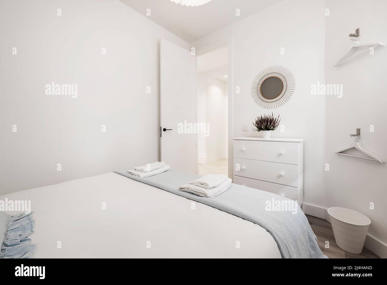 chambre avec lit double avec serviettes blanches pliées, commode blanche, miroir décoratif et cintres blancs Banque D'Images