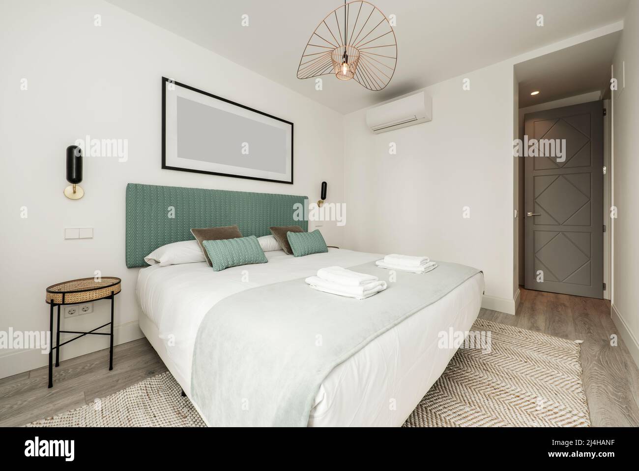chambre avec lit double avec serviettes pliées blanches, tête de lit capitonnée en tissu bleu, coussins assortis et tapis en denim Banque D'Images