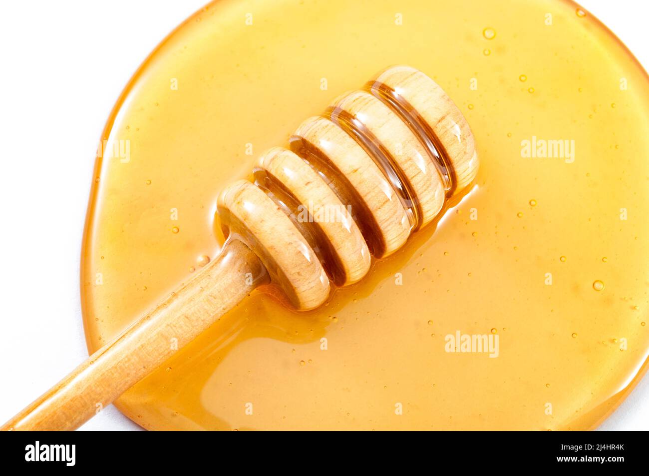 Gros plan sur le miel qui s'égoutte du balancier dans une piscine de miel jaune doux isolée sur blanc Banque D'Images