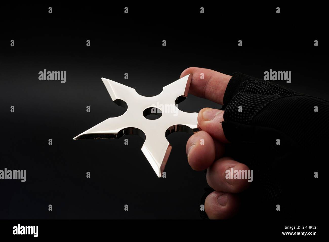 Art martial et traditionnel japonais arme concept avec main dans le gant ninja sans doigts tamer métal en forme d'étoile shuriken isolé sur la ba noire Banque D'Images
