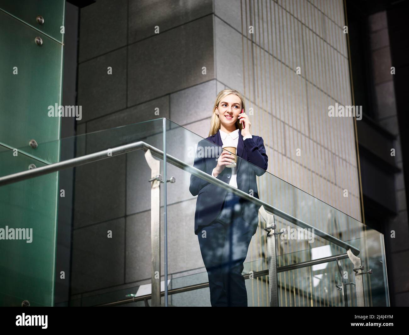 jeune femme d'affaires caucasienne se tenant au-dessus des escaliers faisant un appel en utilisant le téléphone cellulaire dans un immeuble de bureau moderne Banque D'Images