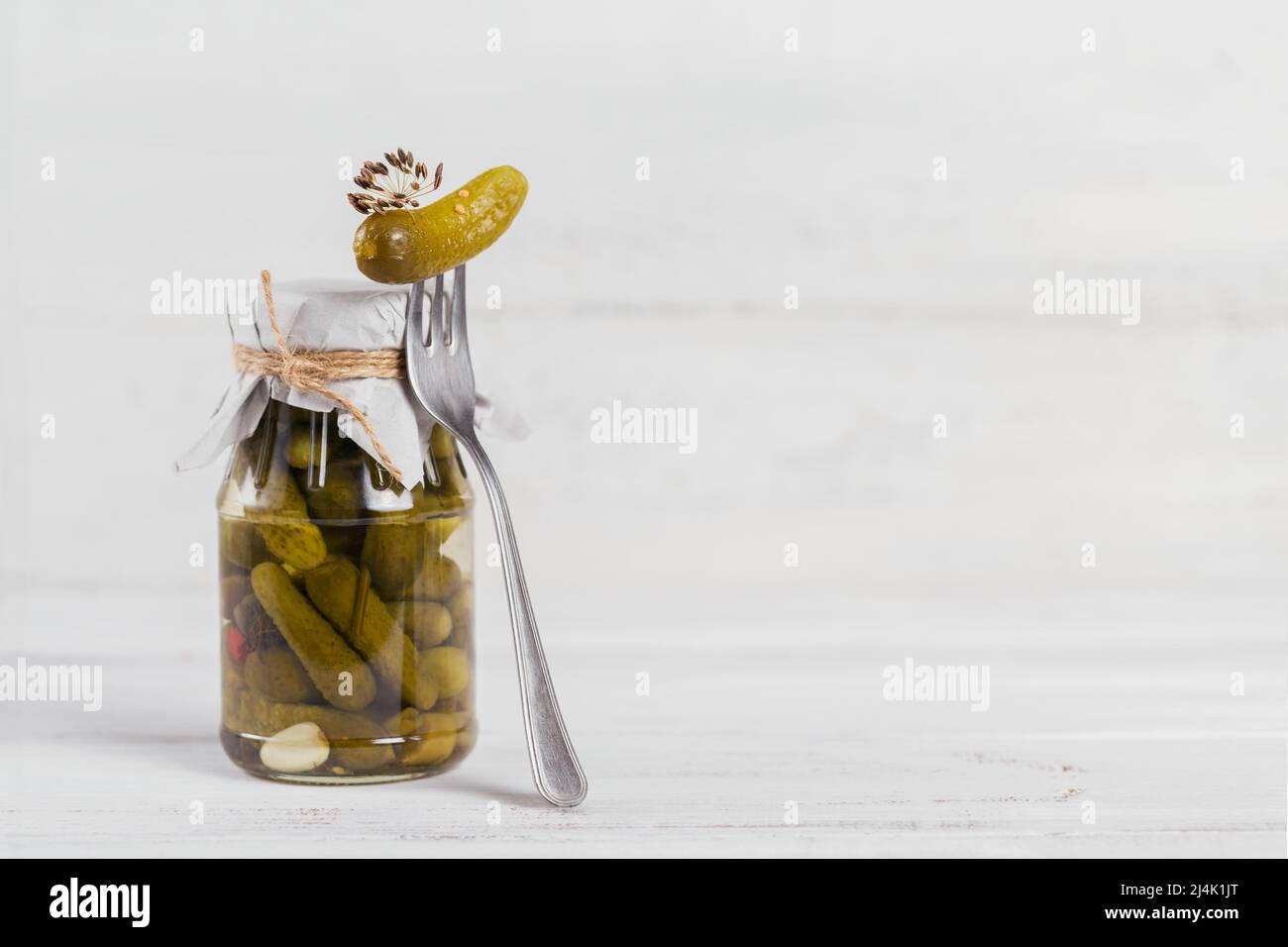 Cornichons, concombre mariné sur une fourchette, légumes marinés dans un pot en verre sur fond de bois blanc Banque D'Images