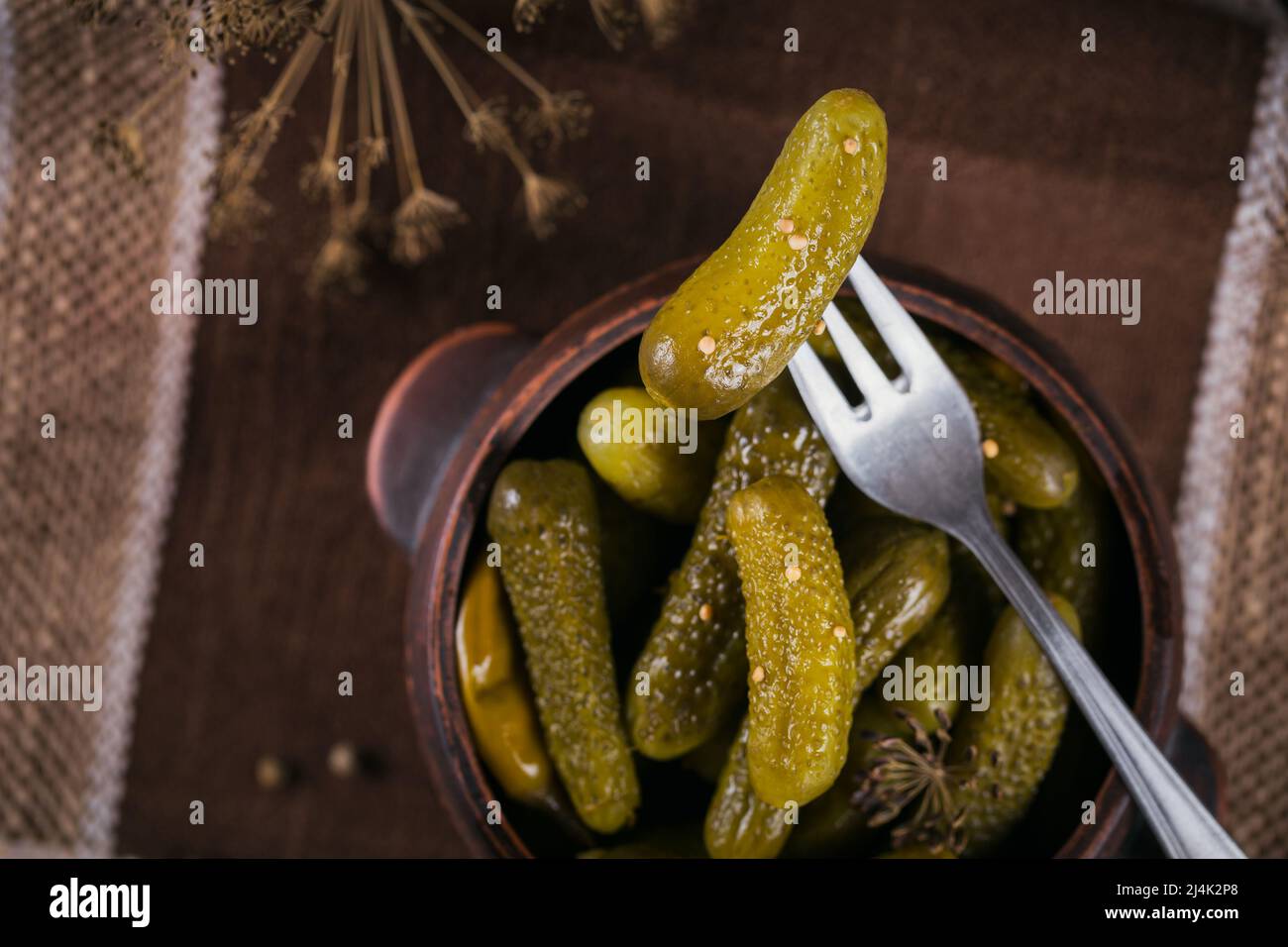 Cornichons, concombre mariné sur une fourchette, bol de légumes marinés sur un fond rustique en bois Banque D'Images