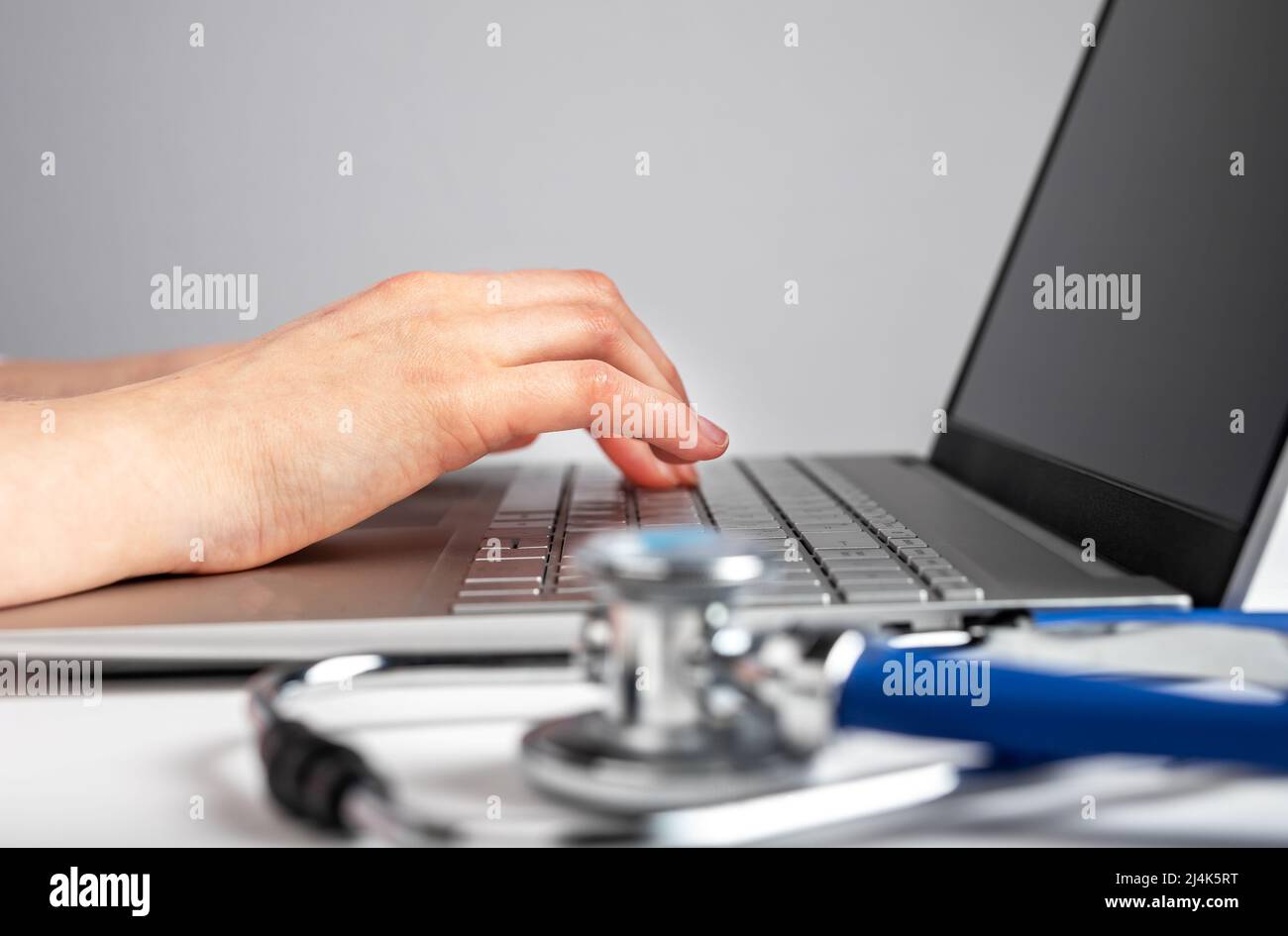 Les mains du médecin tapent de près sur le clavier de l'ordinateur portable. Femme assise au bureau avec ordinateur et stéthoscope et prenant des notes sur le diagnostic du patient, le traitement . Photo de haute qualité Banque D'Images