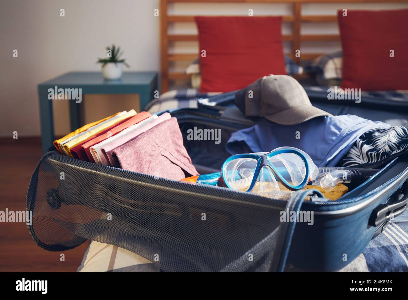 Valise ouverte avec vêtements d'été et lunettes de plongée sur le lit à la maison. Emballage et planification voyage aventure. Banque D'Images