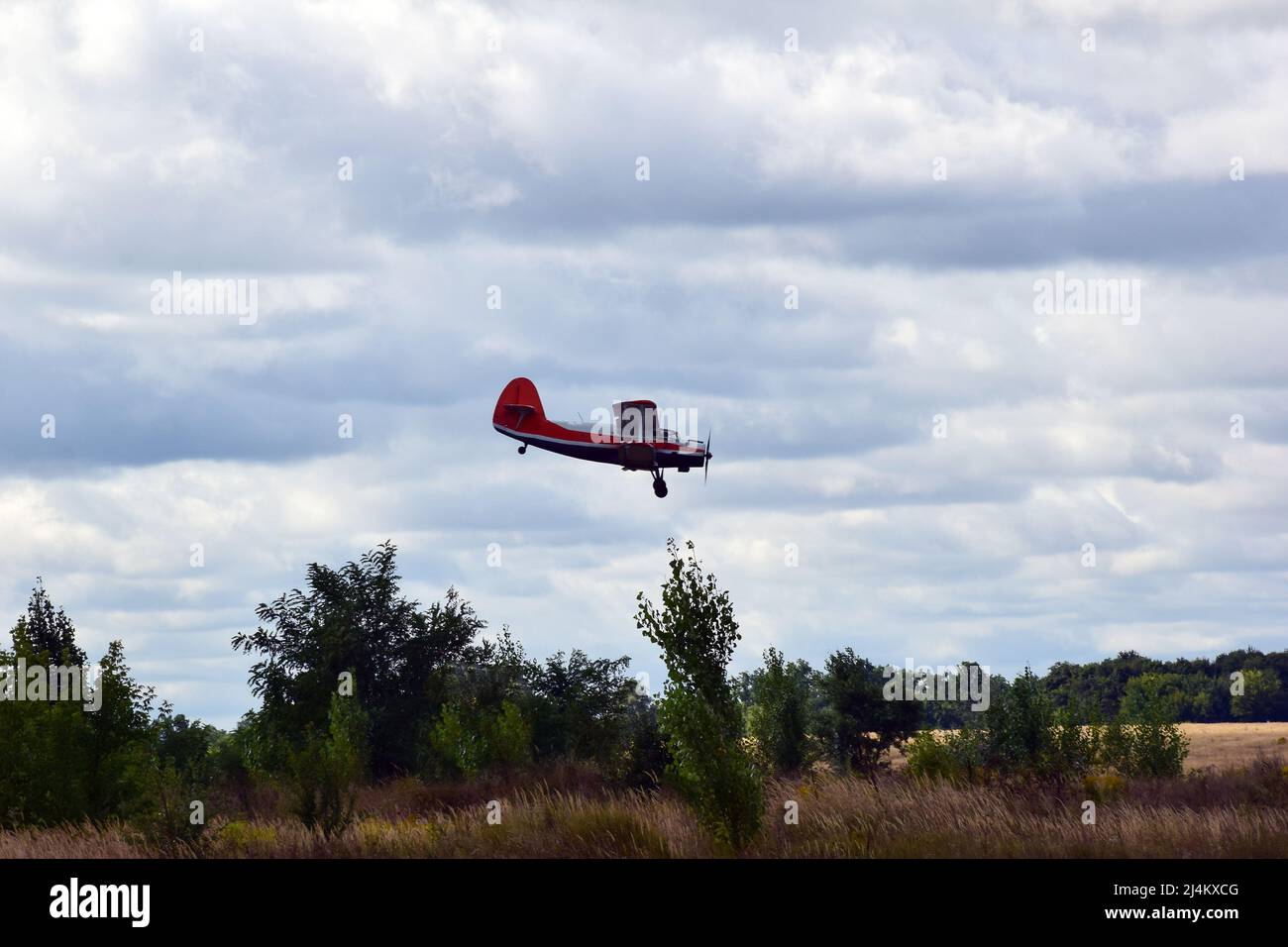 Un ancien avion biplan avec hélice descend pour atterrir dans un ciel bleu nuageux Banque D'Images